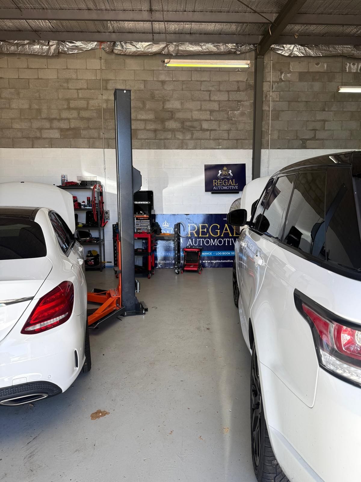 Inside the Regal Automotive workshop in North Albury, with two cars in the service bays, tool trolleys along the back wall and the branded Regal Automotive banner and sign